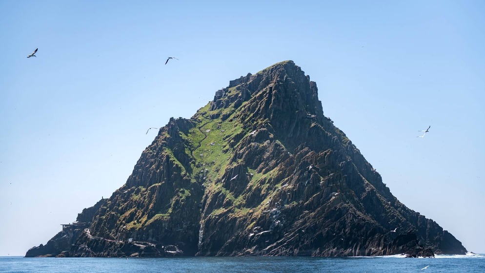 Rocky, grass-covered peak of Skellig Michael rises sharply from the Atlantic, with seabirds soaring overhead.