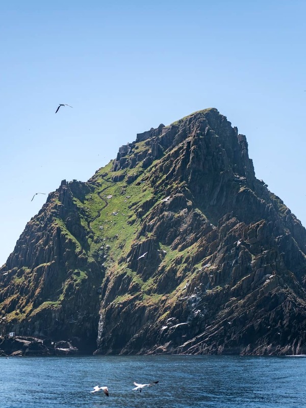 Rocky, grass-covered peak of Skellig Michael rises sharply from the Atlantic, with seabirds soaring overhead.