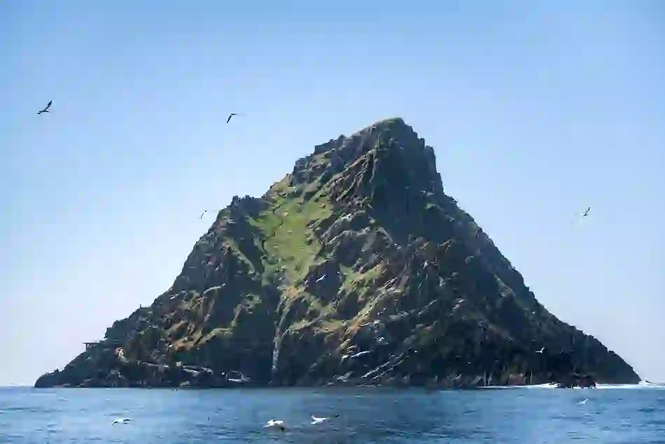 Rocky, grass-covered peak of Skellig Michael rises sharply from the Atlantic, with seabirds soaring overhead.