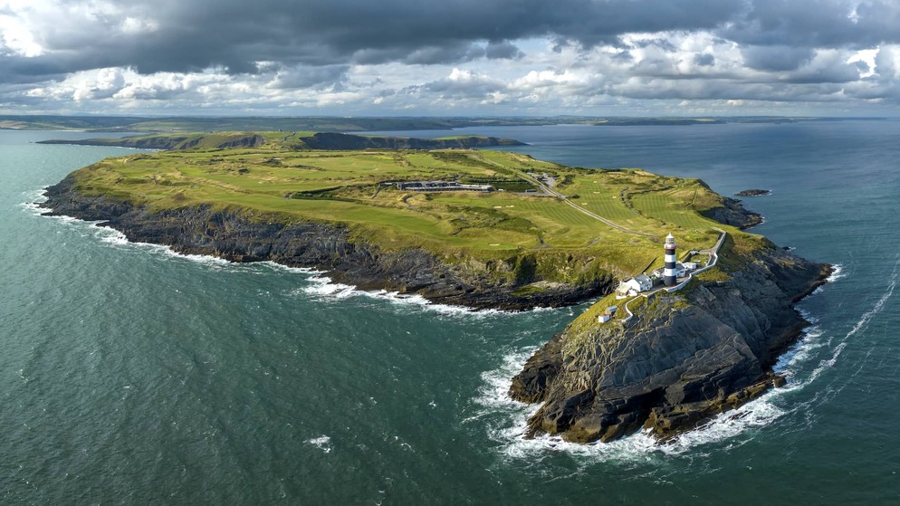 Aerial view of the Old Head of Kinsale lighthouse perched on a dramatic headland jutting into the Atlantic Ocean.