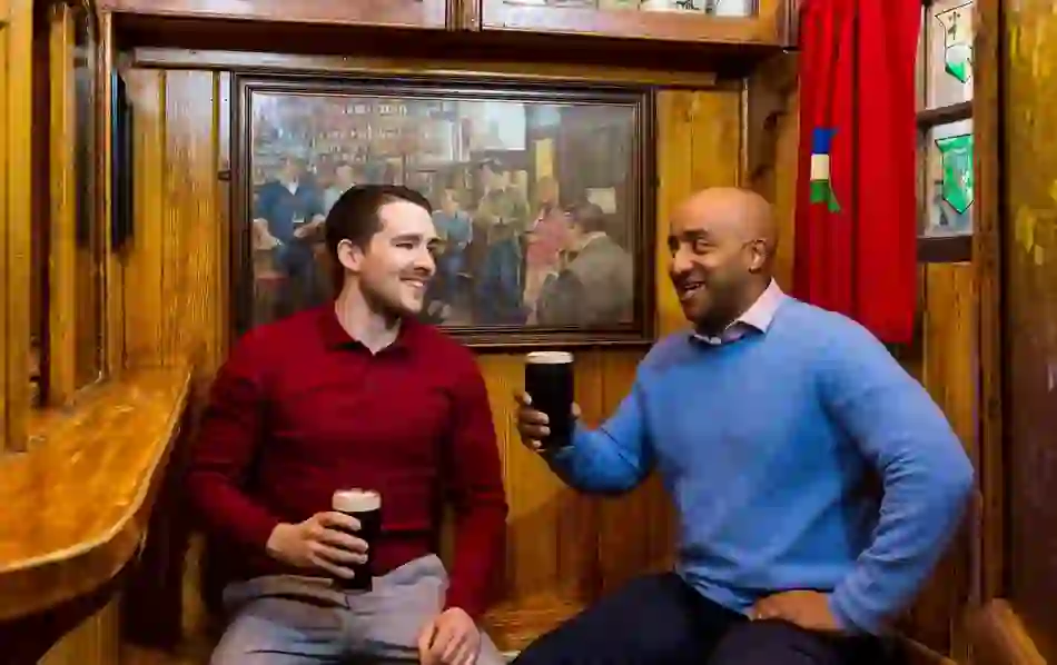 Two men enjoying pints of stout inside the cosy wooden booths of Dick Mack’s pub in Dingle.