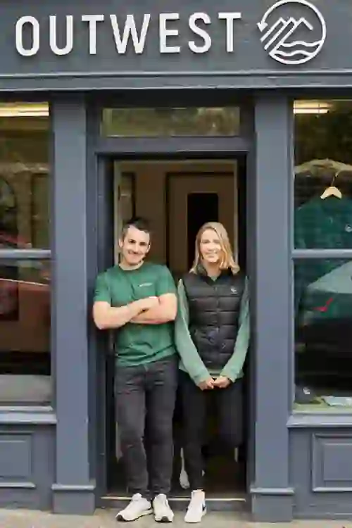 Two people stand at the entrance of Outwest shop in Dingle, County Kerry, smiling at the doorway.