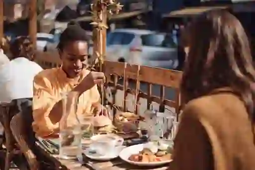 Two women enjoy brunch and coffee at a sunny outdoor café table in Dalkey, with plates of fresh food and relaxed smiles.