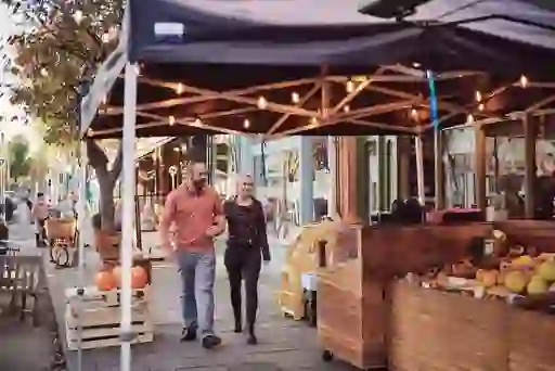 A couple stroll past a street market with fruit stands and autumn decorations in lively Glasthule village.