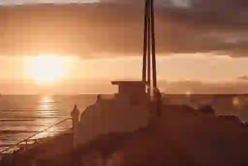Silhouetted visitors watch the sunset beside Bull Island on the Dublin coast, sky glowing with golden light.