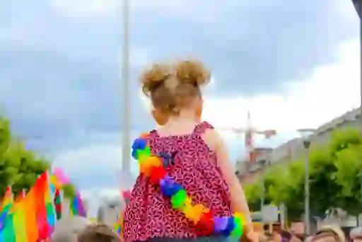 Child wearing a rainbow lei at Dublin Pride parade with flags in the background.