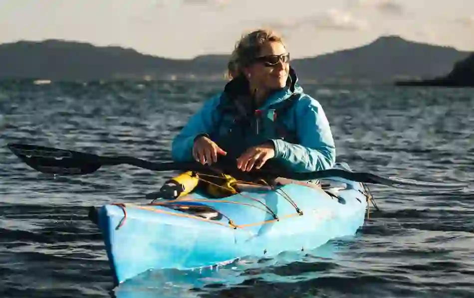 Kayaker wearing sunglasses sitting in blue kayak on Dublin Bay with Howth peninsula in the distance.