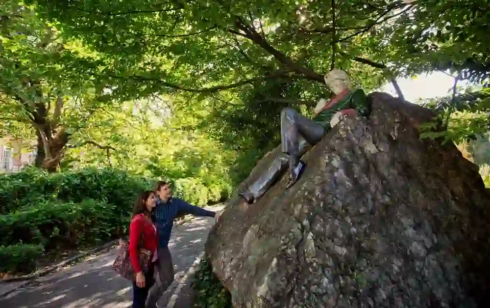 Couple admiring the Oscar Wilde statue on a large rock in Dublin’s Merrion Square Park.