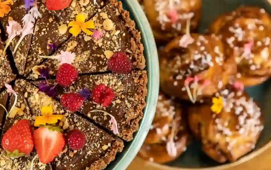 Close-up of chocolate tart topped with strawberries, raspberries and edible flowers beside pastries.