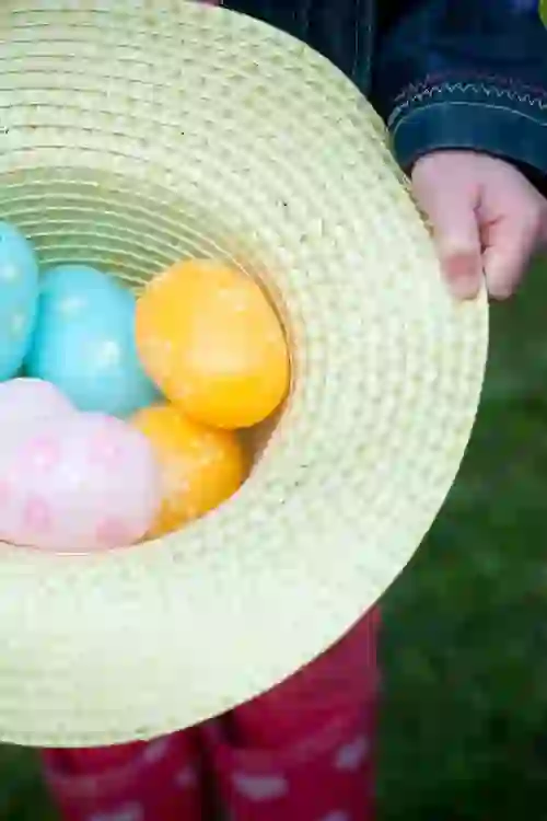 Child holding a straw hat filled with colourful painted Easter eggs.