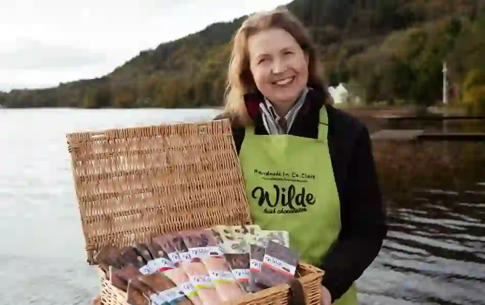 Smiling woman with basket of Wilde Irish Chocolates by a lakeside in County Clare.