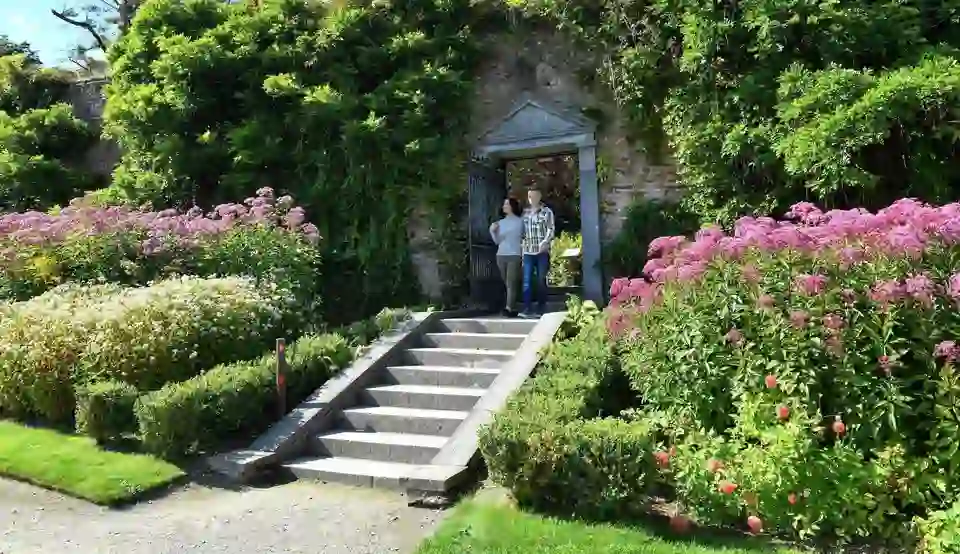 Couple walking through a stone archway surrounded by vibrant summer blooms at Mount Congreve Gardens, County Waterford.