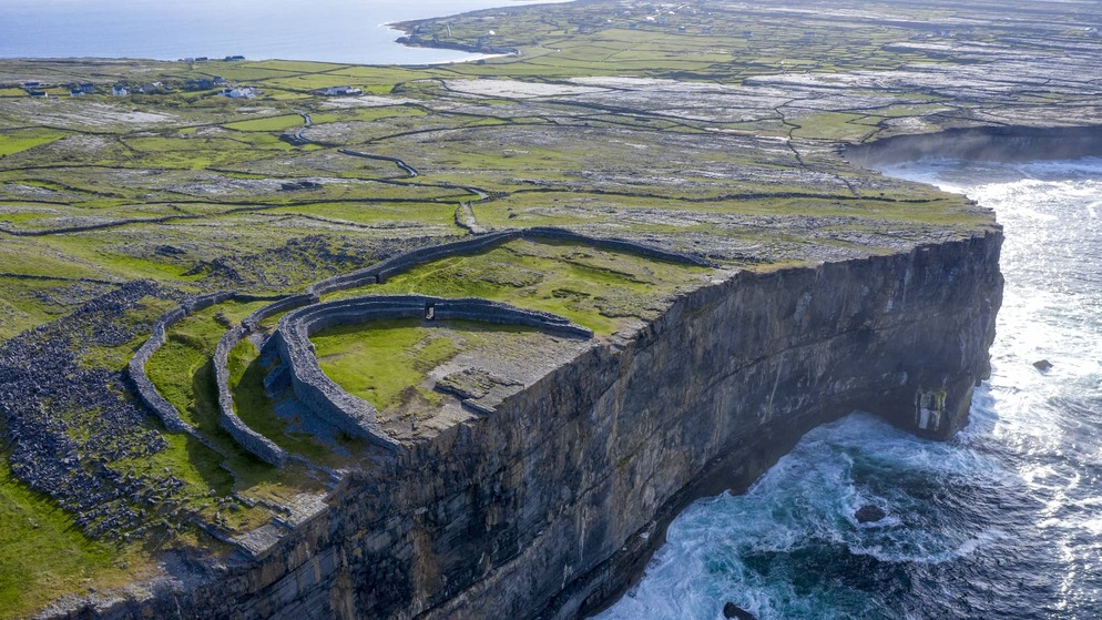 Ancient stone fort perched on sea cliffs of the Aran island of Inis Mór, County Galway surrounded by green fields and rugged Atlantic coastline.