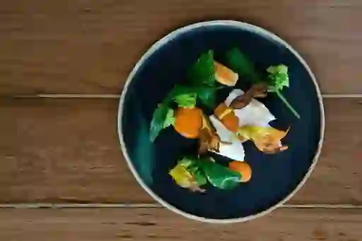 A modern dish of seasonal vegetables artfully arranged on a dark plate set on a wooden table.