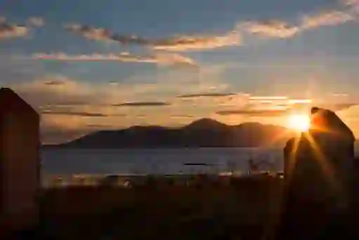 Sunset over the sea viewed between two stone ruins, with the Mourne Mountains in silhouette.