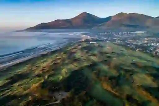 Aerial view of a lush golf course stretching to the coastline, with the Mourne Mountains in the distance.