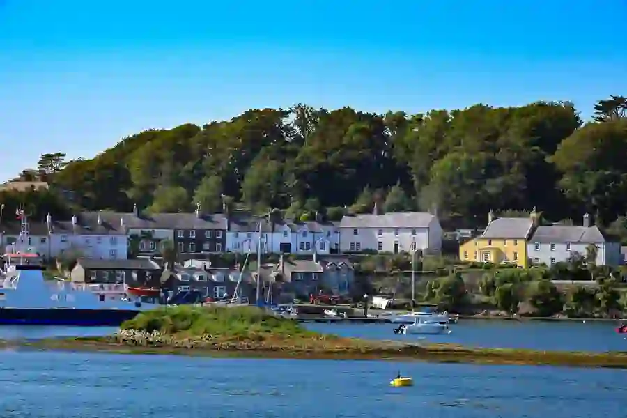 Colourful houses line the edge of a wooded shoreline beside calm waters and clear blue skies.