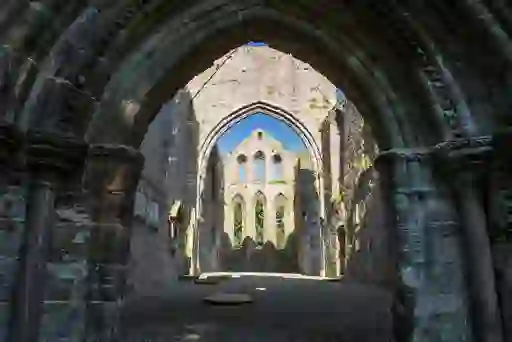 Gothic stone archways and windows of a medieval abbey ruin with sunlight filtering in.