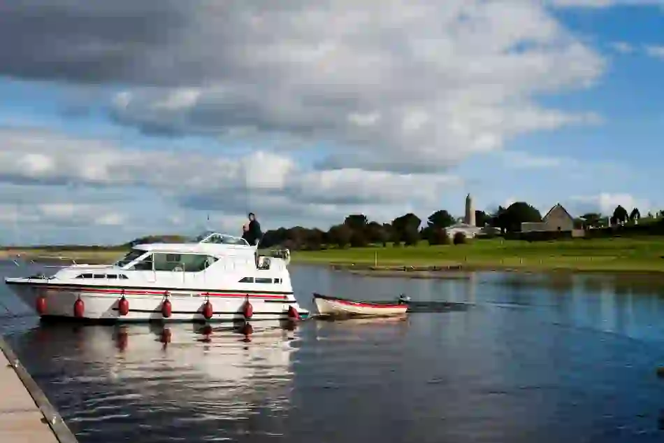 Boat cruising on the River Shannon near Clonmacnoise monastic site with round tower in the distance.