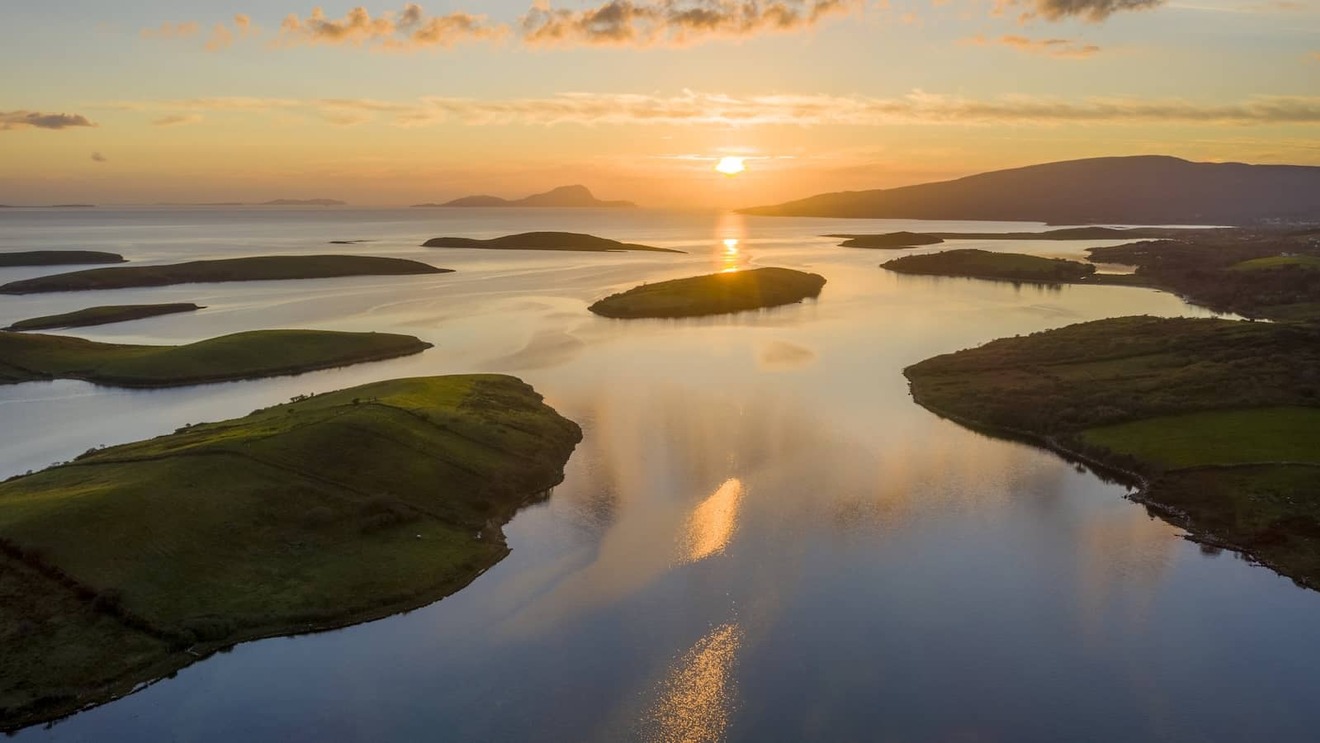 Aerial view of Clew Bay at sunset, County Mayo, with scattered islands and golden light reflecting on calm water.