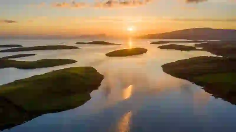 Aerial view of Clew Bay at sunset, County Mayo, with scattered islands and golden light reflecting on calm water.