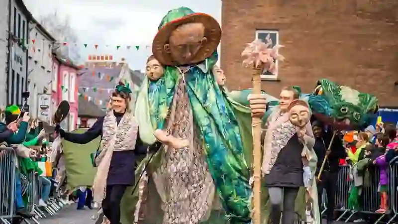 Giant green-cloaked figure leads St Patrick’s Day parade through Kilkenny streets lined with spectators.