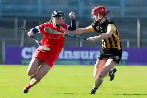 Intense camogie match with players in red and black-and-amber jerseys competing for the sliotar.