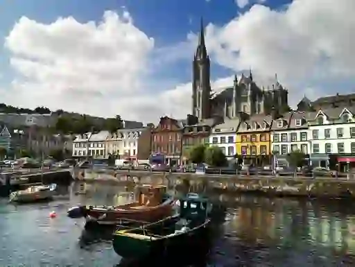 Boats moored at Cobh harbour with colourful houses and St Colman’s Cathedral in the background.