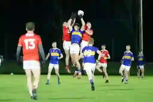 Tipperary and Cork players leap simultaneously for the ball in a high catch during McGrath Cup Gaelic football match.