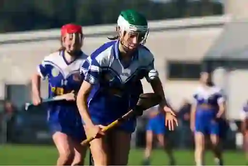 Camogie player in blue and white soloing with sliotar during a senior championship game in Cork.