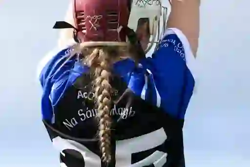 Camogie player from Na Sáirséalaigh club in helmet and jersey prepares to strike during a semi-final match in Cork.