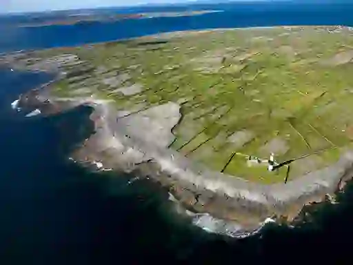 Aerial view of Aran Islands coastline with patchwork stone-walled fields and lighthouse near the shore.