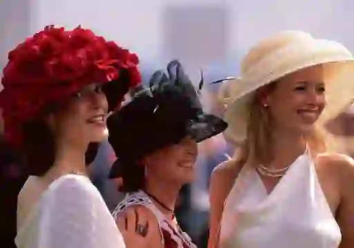 Three women in elegant hats and dresses smile while attending Ladies’ Day at the Galway Races.
