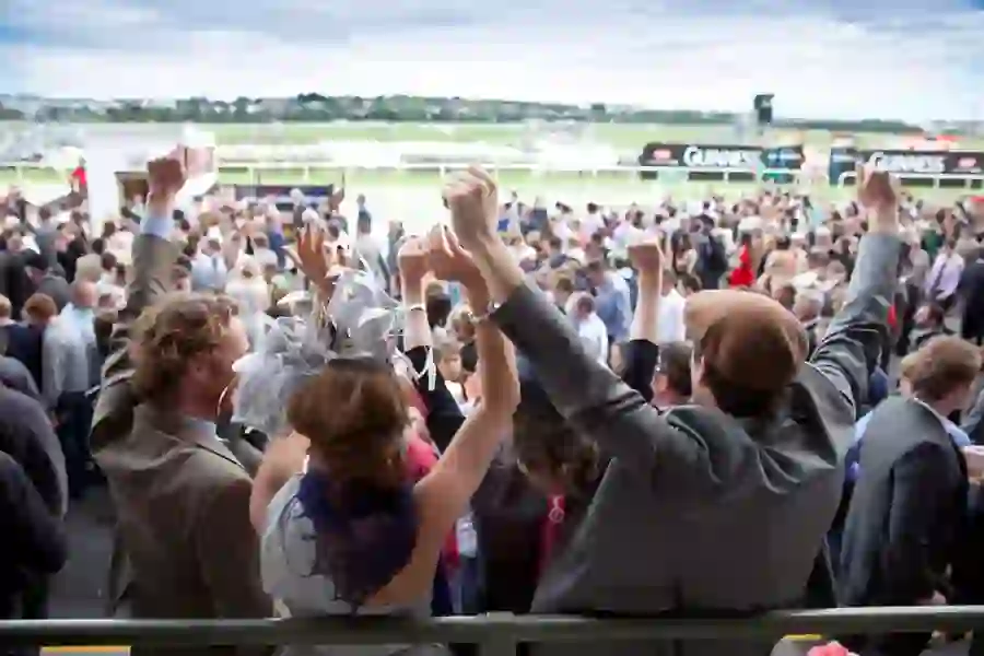 Excited racegoers cheer from the stands at Galway Races, overlooking the busy track and crowds.