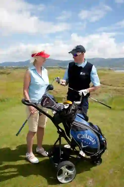 Two golfers chatting beside a golf bag at Waterville Golf Course in County Kerry with mountains in the background.