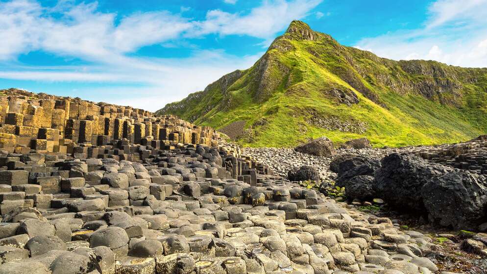 Hexagonal basalt columns rising below a grassy peak on the Giant’s Causeway World Heritage Site trail.