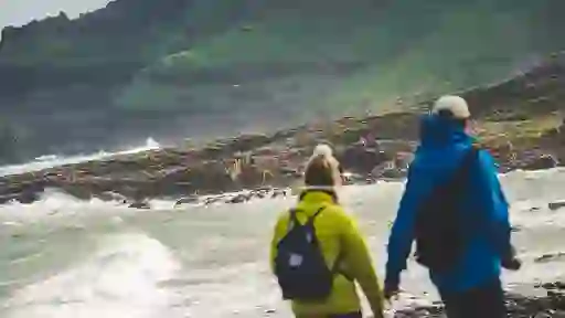 Two walkers in bright jackets on a windswept beach near Giant’s Causeway basalt rocks in County Antrim.