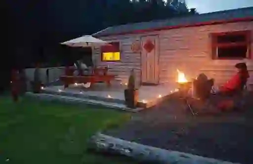 A wood cabin with firepit and guests seated outside at dusk at Ox Mountain Adventure Camp, County Sligo.
