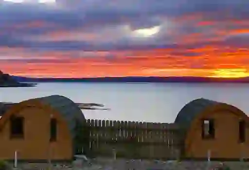 Wooden glamping pods on Rathlin Island, County Antrim, face a vibrant sunset over the sea.