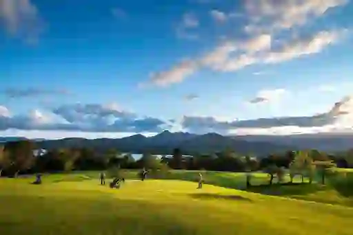 Golfers on the green at Glengarriff Golf Club overlook Bantry Bay with mountains rising in the background.