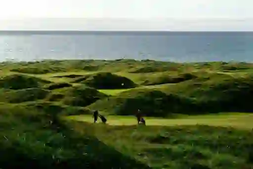 Golfers walk the rugged fairways of Strandhill Golf Club with the Atlantic Ocean stretching beyond the course.