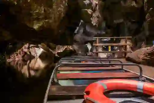 Wooden boat inside Marble Arch Caves floating on dark underground river below rock formations.