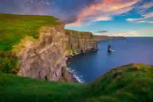 Cliffs of Moher stretching along the Atlantic coast at sunset, sheer rock faces meeting deep blue ocean waves.