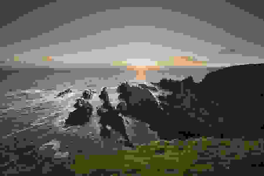 Sun setting behind jagged cliffs and crashing waves on the scenic Cork coastline.