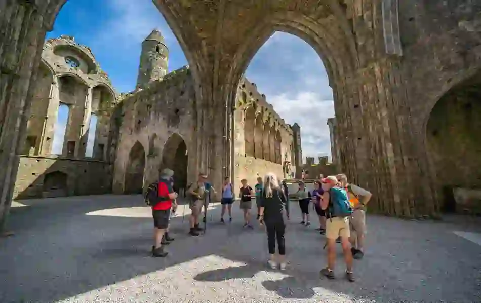 Visitors touring the Rock of Cashel’s medieval cathedral ruins beneath towering Gothic arches on a sunny day in Tipperary.