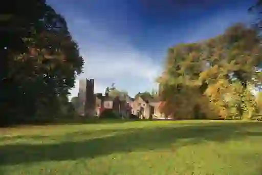 Autumn trees surround Belle Isle Castle manor with ivy-covered walls under a dramatic blue sky.