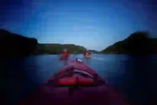 Kayakers paddling across the still waters of Lough Hyne, County Cork at twilight, surrounded by forested hills.