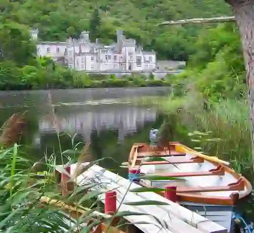 View of Kylemore Abbey reflected in its tranquil lake, framed by lush green trees and a small wooden boat in the foreground.