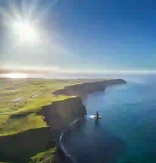 Aerial panorama of the Cliffs of Moher in County Clare, towering over the Atlantic Ocean beneath a bright sunlit sky.