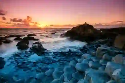Sunset over the Giant’s Causeway with hexagonal stone columns and waves crashing on the shore.